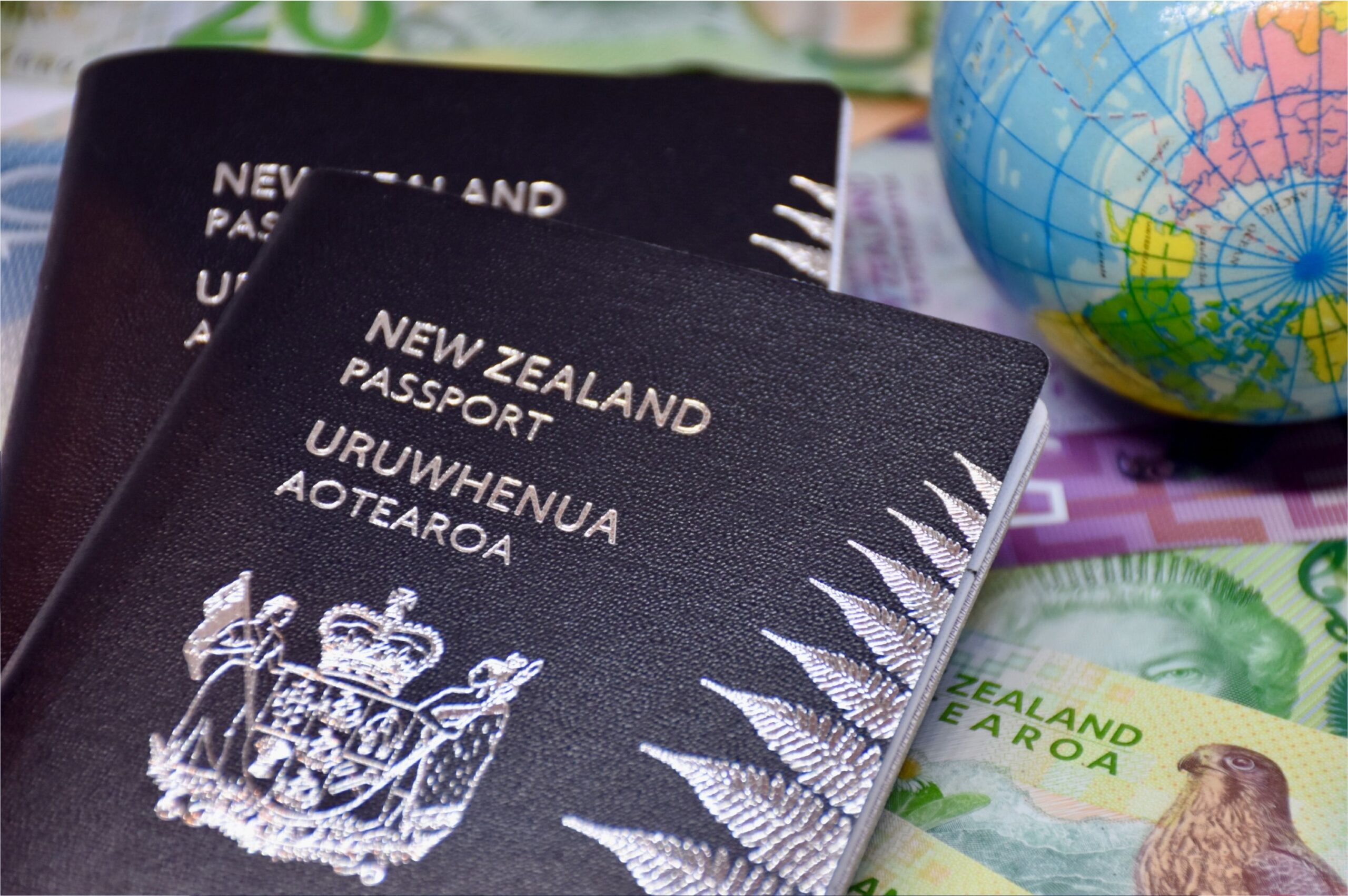 Pasaportes de Nueva Zelanda junto a un globo terráqueo y moneda neozelandesa