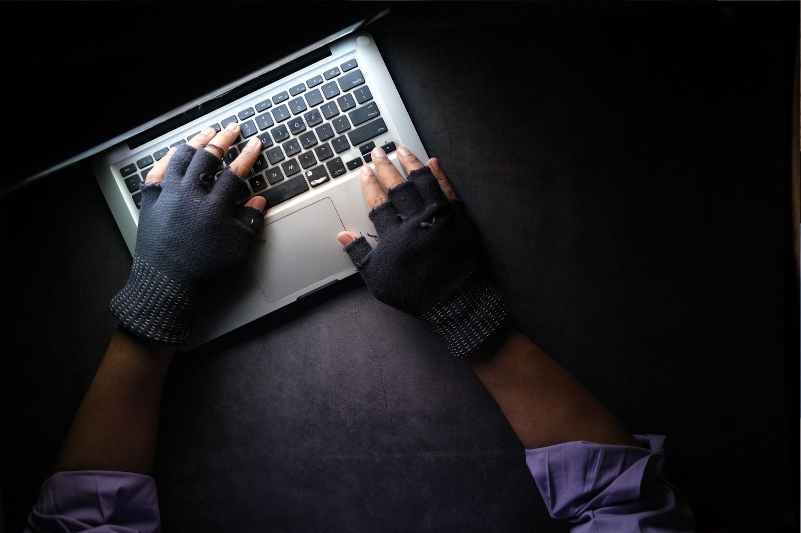 Persona encapuchada utilizando un ordenador portátil, símbolo de fraude en Internet